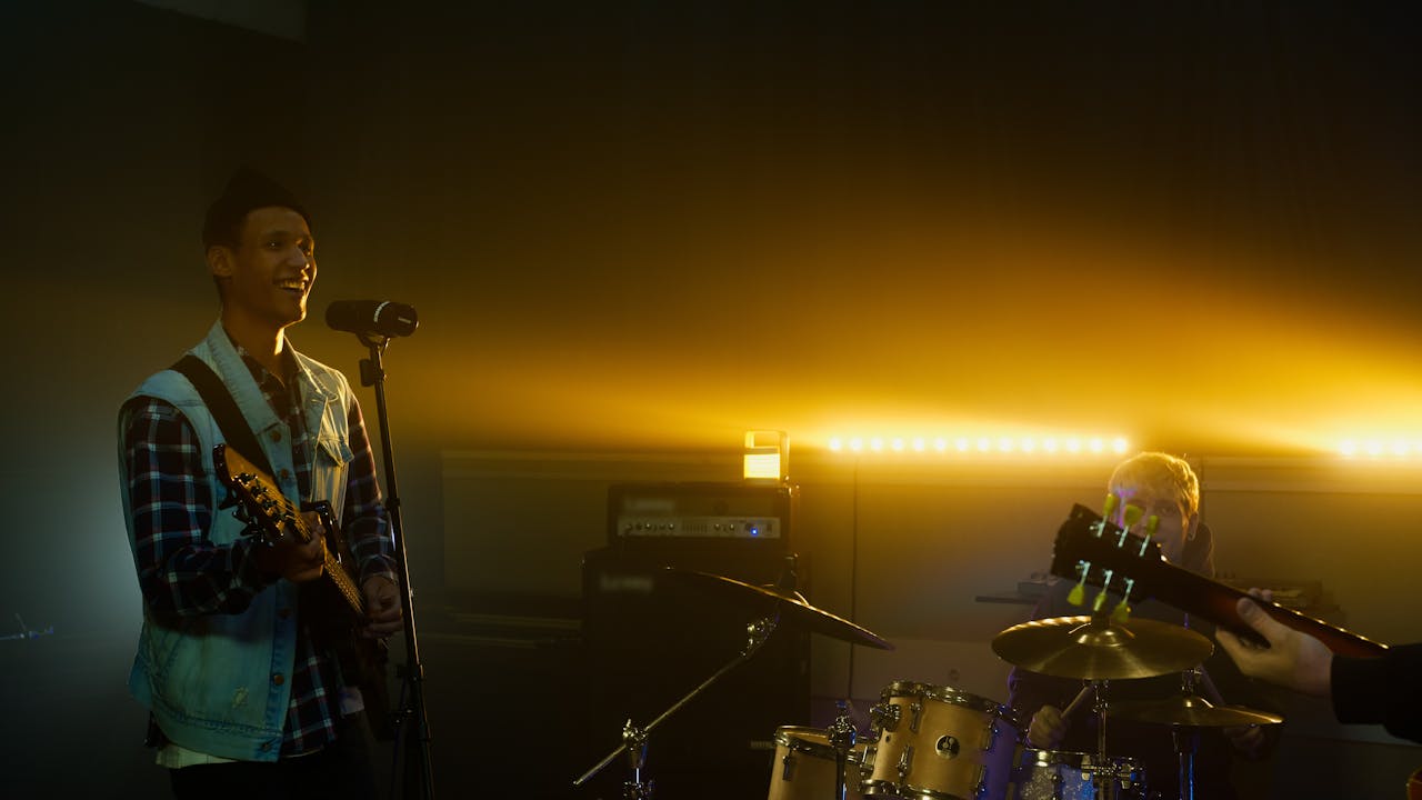 A band performing with vibrant lighting in a dimly lit venue, featuring a guitarist and drummer.